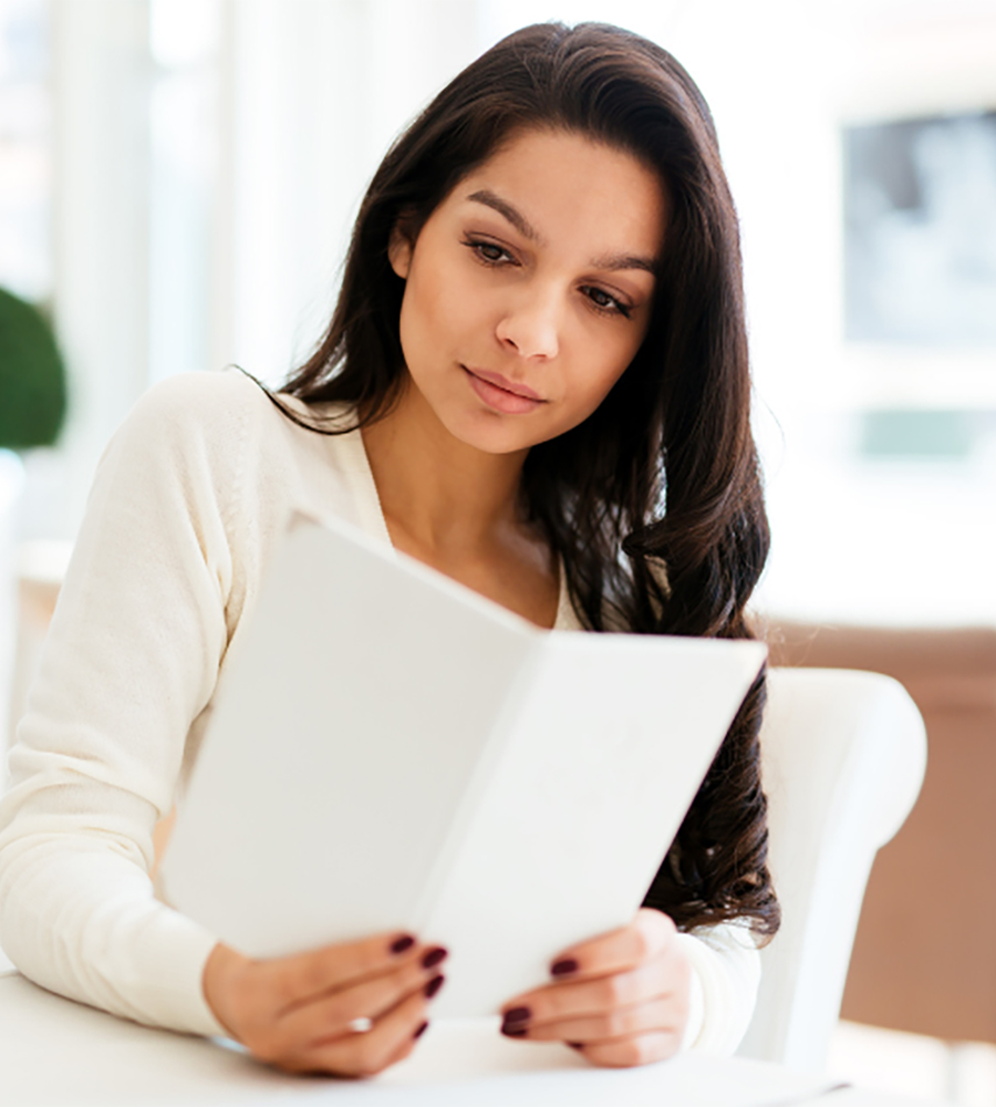 A woman sitting at a table reading a paper.